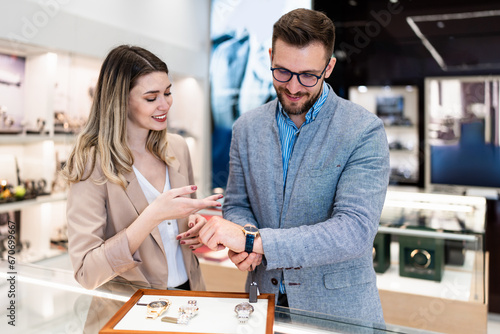 Elegant middle age businessman choosing and buying his new expensive watch. Beautiful young female seller helps him to make good decision. Fashion style and elegance concept. photo