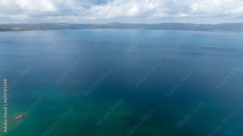 Aerial view of Lake Bracciano, originally also called Lake Sabatino. It is a lake of volcanic and tectonic origin, located in the metropolitan city of Rome and surrounded by the Sabatini Mountains. Aerial view of Lake Bracciano, originally also called Lake Sabatino. It is a lake of volcanic and tectonic origin, located in the metropolitan city of Rome and surrounded by the Sabatini Mountains.