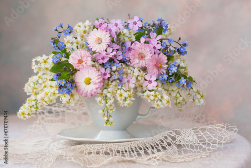 A bouquet of spring flowers: bird cherry, daisies, forget-me-nots in a cup on the table, a beautiful composition, still life, a holiday card.