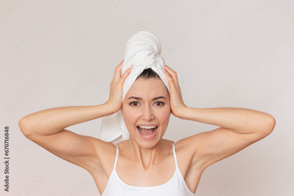 young pretty woman in white underwear with a white towel on her head presses hands to her head, spreading her elbows to the sides, screams, covering her ears. Isolated on a beige background young pretty woman in white underwear with a white towel on her head presses hands to her head, spreading her elbows to the sides, screams, covering her ears. Isolated on a beige background