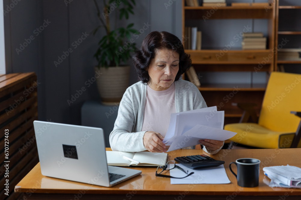 Middle aged senior woman sit with laptop and paper document, Pensive older mature lady reading paper bill pay online at home managing bank finances calculating taxes planning loan debt pension payment Middle aged senior woman sit with laptop and paper document, Pensive older mature lady reading paper bill pay online at home managing bank finances calculating taxes planning loan debt pension payment