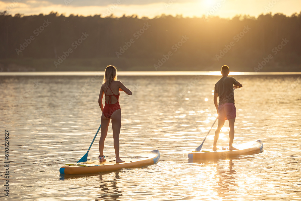 Man and woman sup board surfers at sunset.