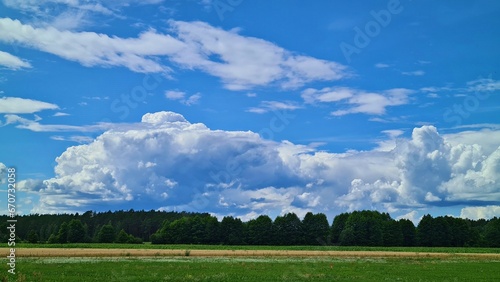 White cumulus clouds on blue light sky and wide green field