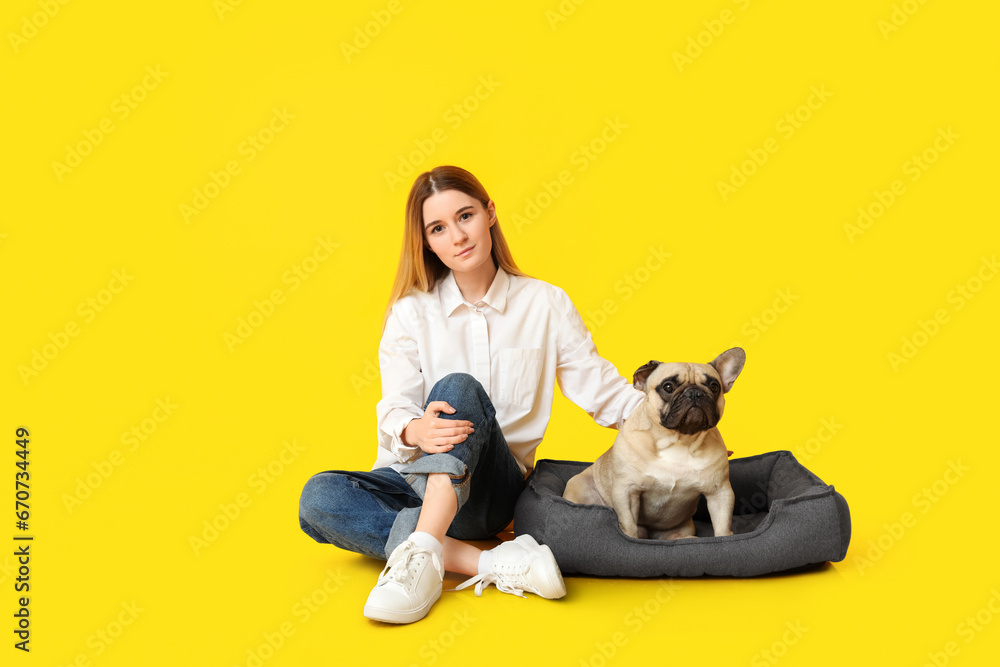Beautiful young woman and cute pug dog sitting on pet bed against yellow background Beautiful young woman and cute pug dog sitting on pet bed against yellow background