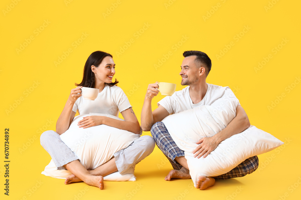 Young couple with cups of coffee and pillows on yellow background Young couple with cups of coffee and pillows on yellow background