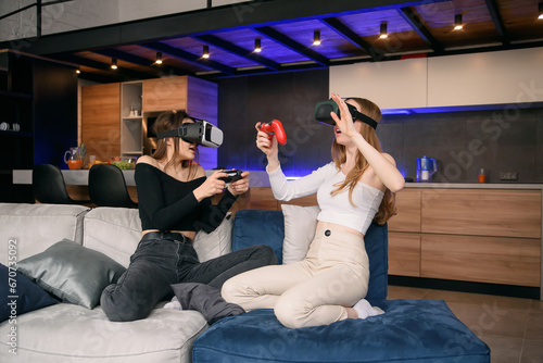 Girlfriends playing with excitement video games at home using vr glasses. Enjoying vacation time to spend leisure with friends. #670735092