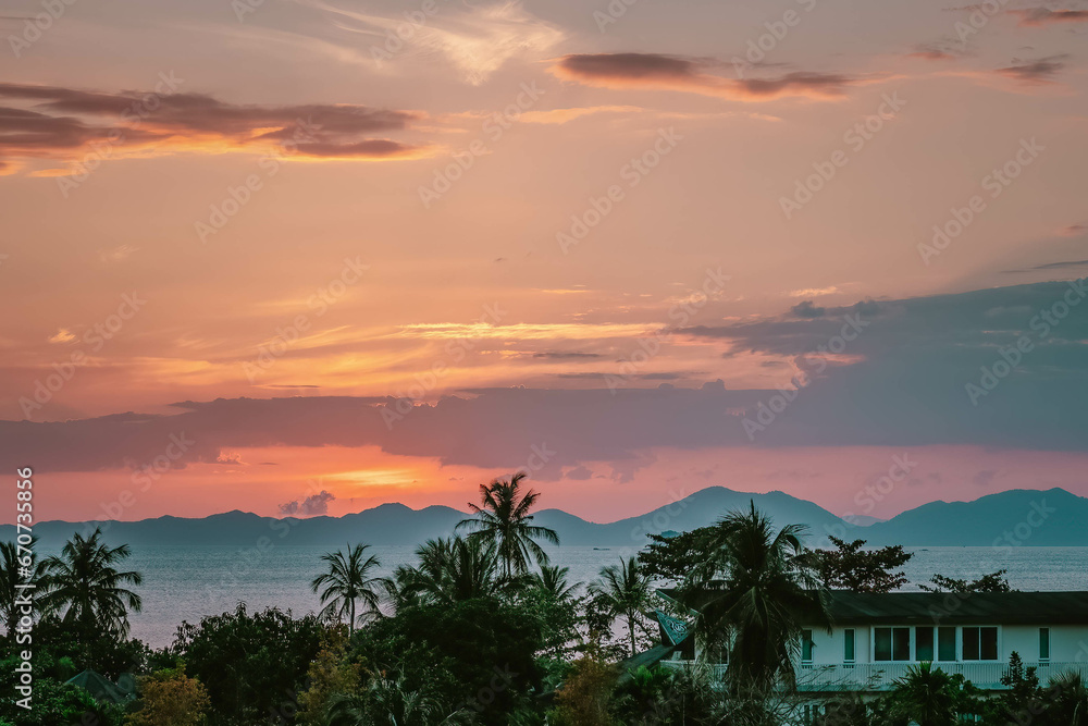 Scenic rose golden glowing Sunset. Sun just hid behind mountains. Close up view on palms, sea and mountains at horizon line. Ao Nang, Thailand