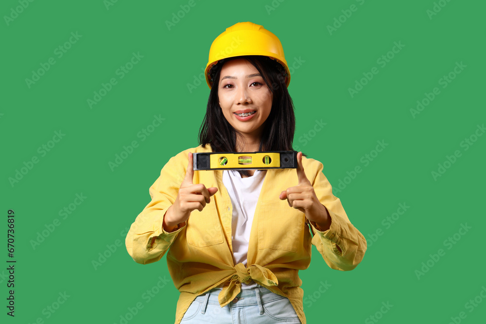 Young Asian woman with building level on green background Young Asian woman with building level on green background