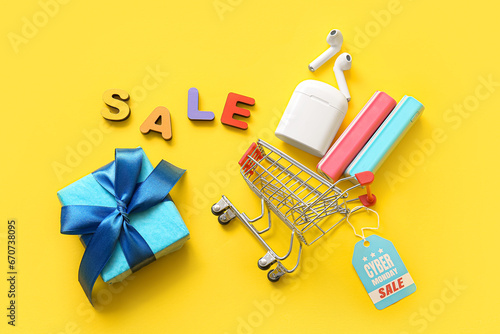 Composition with gadgets, small shopping cart and gift box on yellow background. Cyber Monday sale