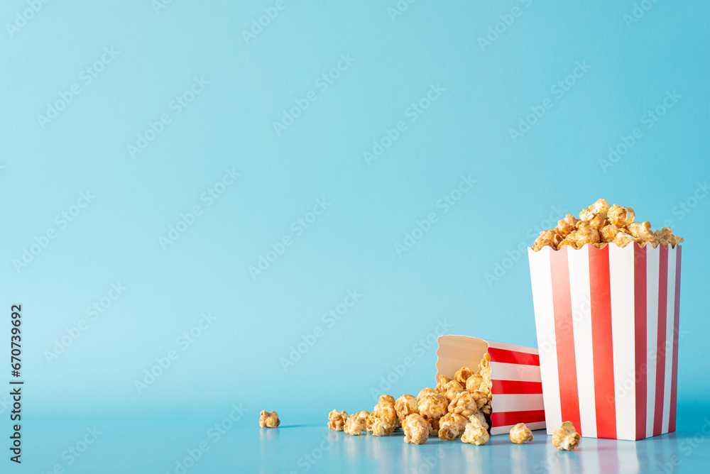 Cherish movie premieres with friends and appetizing snacks. Side view image of a table adorned with delectable popcorn in striped boxes against light blue wall, perfect for movie promotions