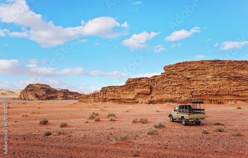 Dusty desert with rocky massif and blue sky above, off road desert vehicle in foreground. Typical scenery in Wadi Rum, Jordan