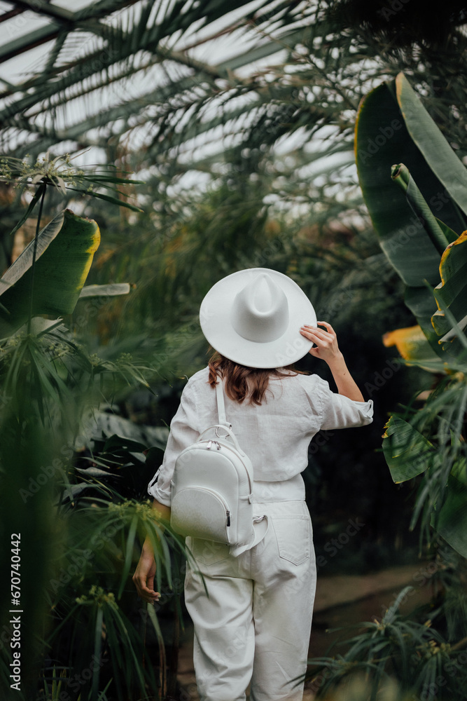 Back view of woman tourist in a hat standing in palm greenhouse of botanical garden