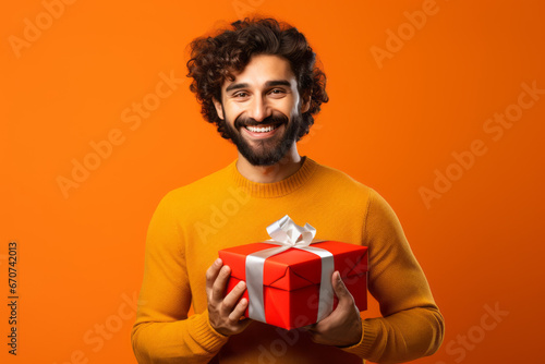Happy smiling man holding gift box Medium shot portrait photography of a grinning mature man holding a gift against a tangerine orange background. © MD Media