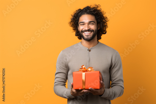 Happy smiling man holding gift box Medium shot portrait photography of a grinning mature man holding a gift against a tangerine orange background. photo