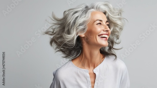 Joyful mature woman with flowing silver hair exudes happiness in a close-up portrait. Her radiant smile highlights her dental health, while her flawless skin  photo