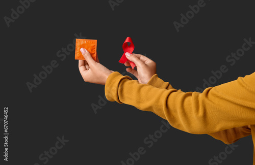 Female hands with red ribbon and condom on black background. World AIDS Day concept