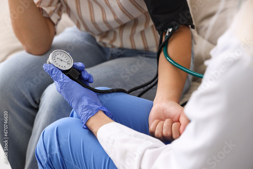 Female doctor measuring blood pressure of patient at home, closeup