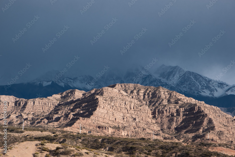 red mountain lit by the sun with gloomy snow-capped mountains on the background