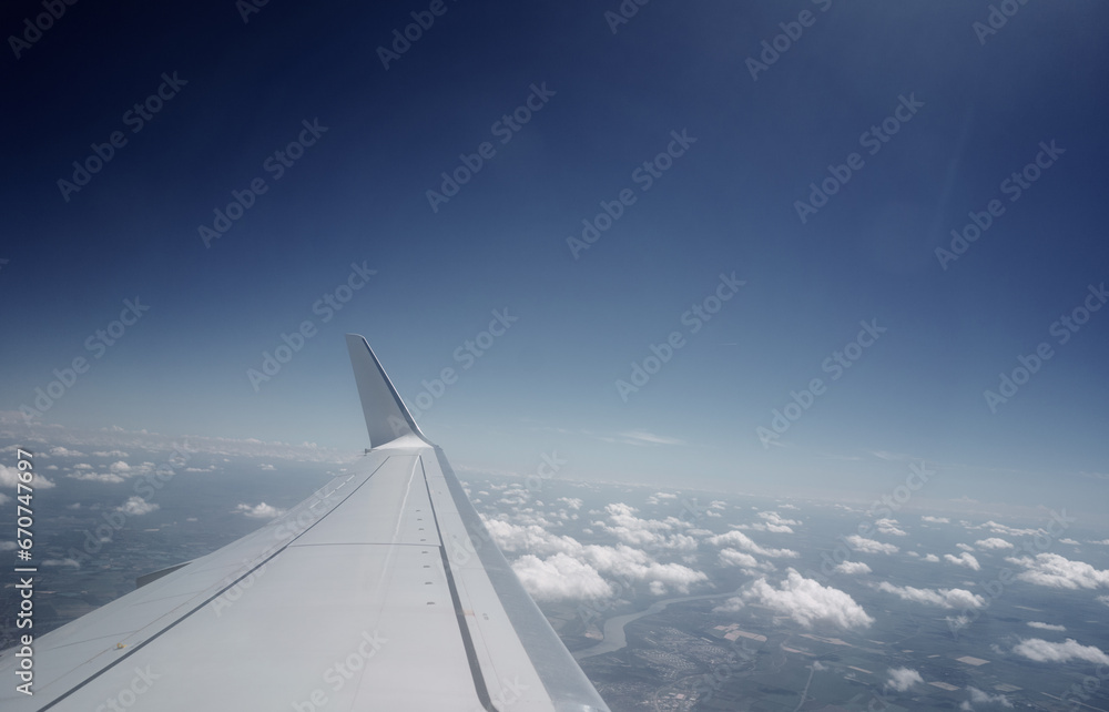 Wing of modern aircraft flying in cloudy blue sky during trip