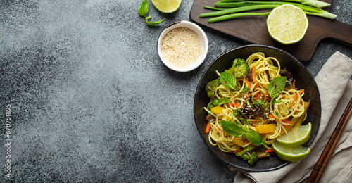 Asian vegetarian noodles with vegetables and lime in black rustic ceramic bowl, wooden chopsticks, cutting board with chopped green onion top view on stone background. Cooking noodles, copy space