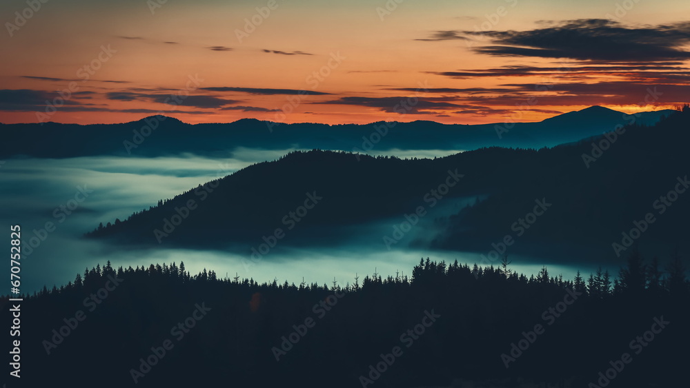 Sunrise sea of fog moving over mountain range, alps mountain silhouette with pine tree forest aerial view. Wild nature mist landscape. Dramatic dark clouds float in orange colored sky