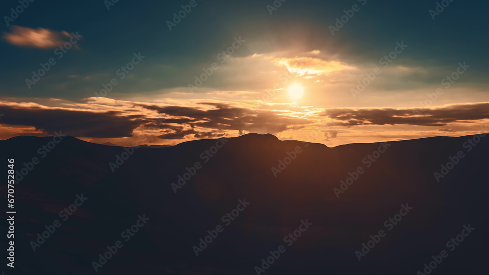 Sunrise cloudscape sky over mountain range silhouette. Dramatic clouds flow in dark sky, sun glow rise over mountain peak with golden light beams. Beautiful morning nature landscape.