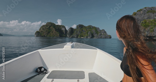 Tourist woman has fun on holiday boat tour to El Nido Islands, Philippines. Long hair girl enjoy ocean mountain wild island landscape sitting on motor boat deck, wind blow hair. Slow motion back view photo