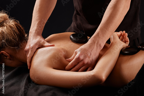 A man receives a hot stone massage, a masseur gives a stone massage
