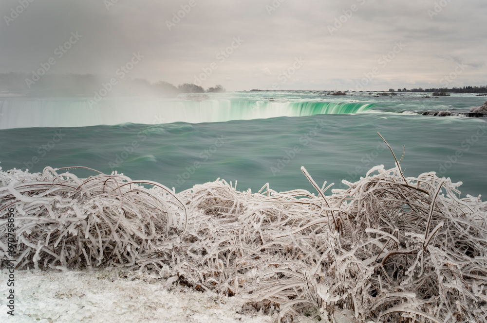 Horizontal cold view of the Niagra Falls among frozen plants and ice on a sad Winter day, Ontario, Canada