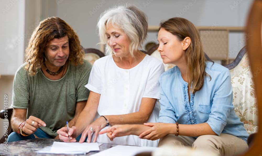 Obraz premium Positive couple and old woman talking about finances and taking notes, resting on the sofa at home