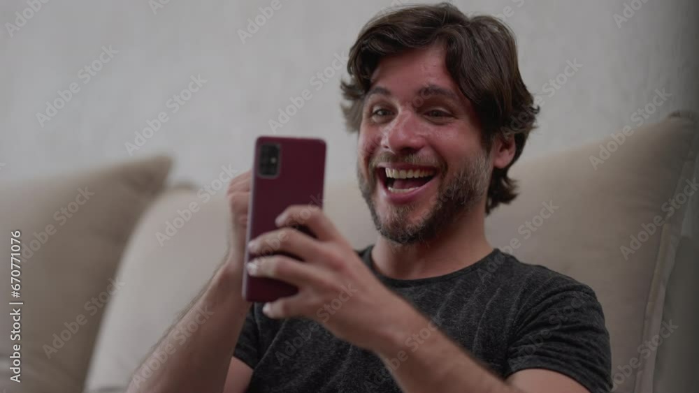 Happy man reacting positively to news notification on cellphone device while sitting at home couch. Ecstatic person celebrating success Happy man reacting positively to news notification on cellphone device while sitting at home couch. Ecstatic person celebrating success