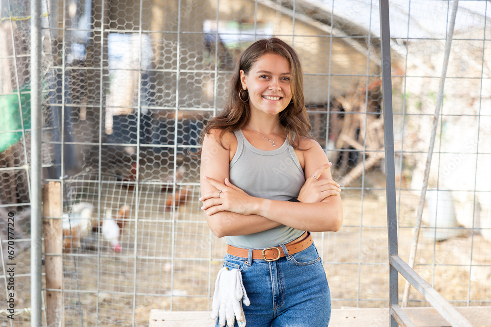 Fototapeta premium Portrait of young happy female farm owner against background of chicken coop