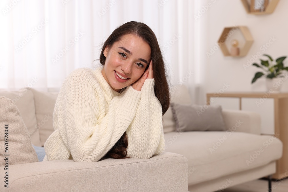 Beautiful young woman in stylish warm sweater on sofa at home, space for text Beautiful young woman in stylish warm sweater on sofa at home, space for text