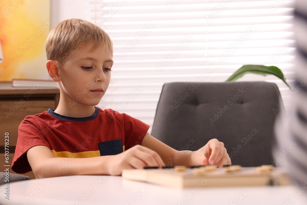 Cute boy playing checkers at coffee table indoors Cute boy playing checkers at coffee table indoors