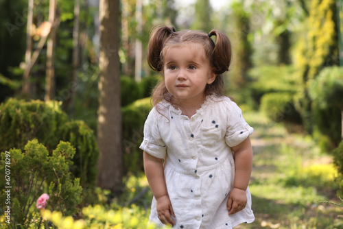 Cute little girl walking near green plants in park