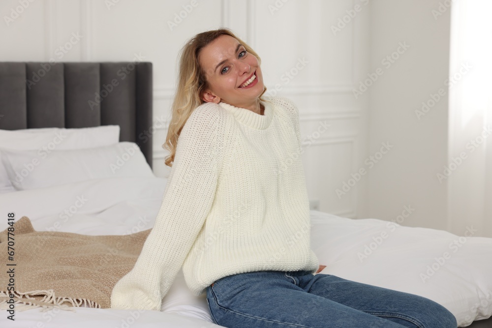 Happy woman in stylish warm sweater on bed at home Happy woman in stylish warm sweater on bed at home