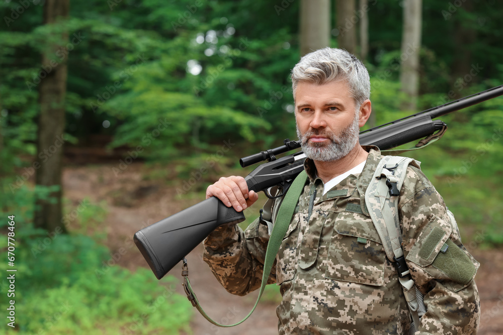 Fototapeta premium Man with hunting rifle wearing camouflage in forest. Space for text