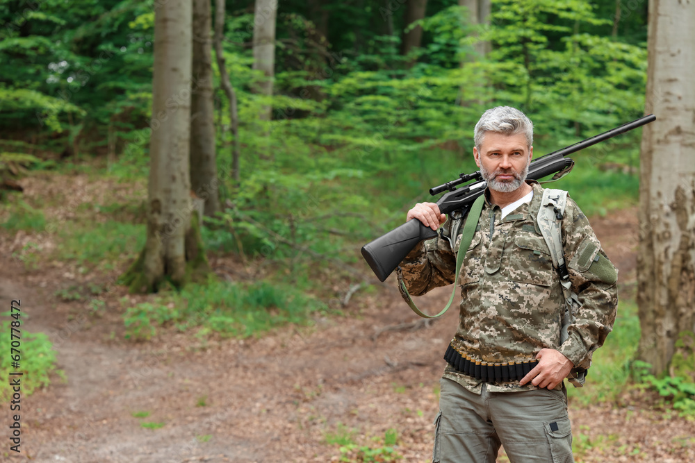 Man with hunting rifle wearing camouflage in forest. Space for text