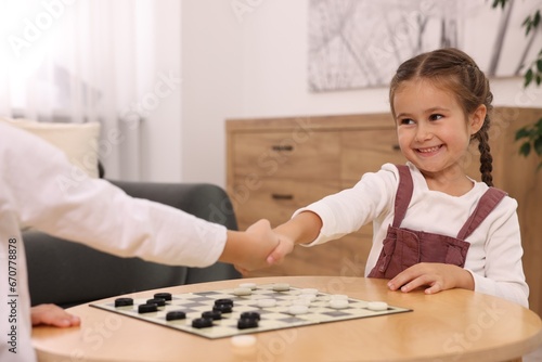 Happy girl shaking hands with her brother after playing checkers at home