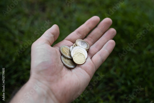 Man hand with euro coins with green grass with sun on background