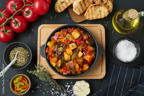 Dish with tasty ratatouille, ingredients and bread on black table, flat lay