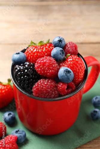 Many different fresh ripe berries in mug on wooden table, closeup