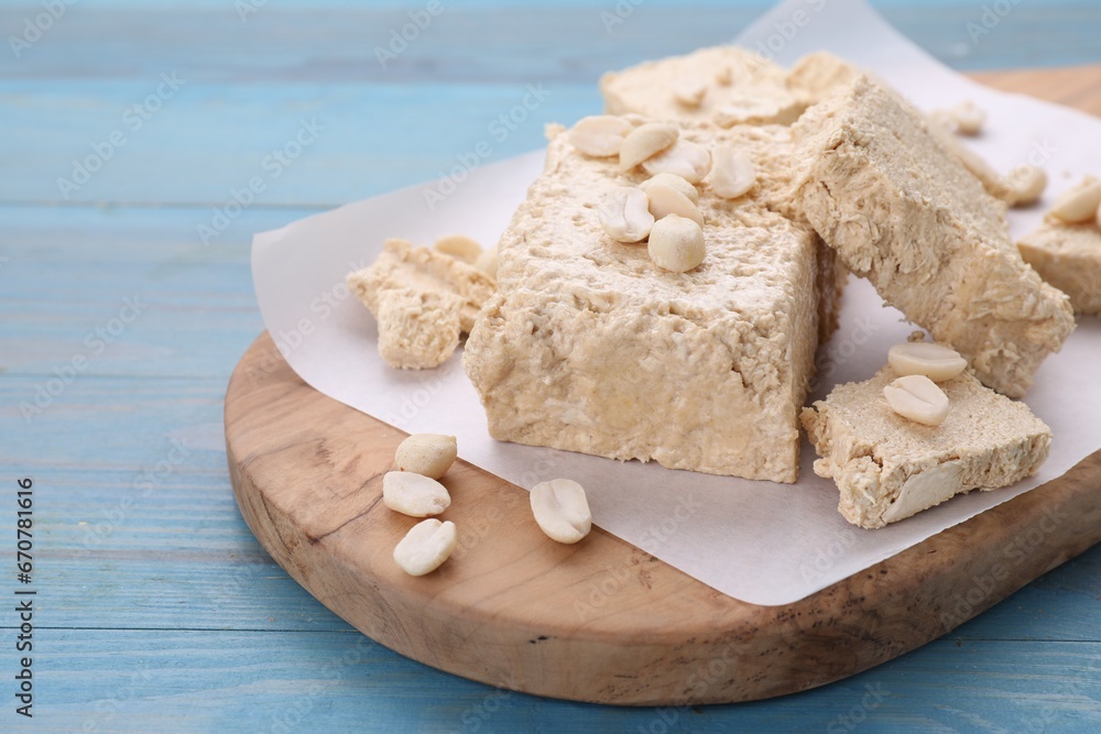 Pieces of tasty halva and peanuts on light blue wooden table, closeup. Space for text
