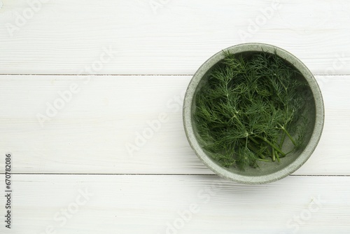 Bowl of fresh green dill on white wooden table, top view. Space for text