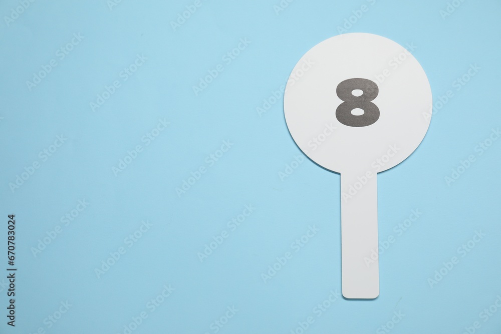 Auction paddle with number 8 on light blue background, top view. Space for text Auction paddle with number 8 on light blue background, top view. Space for text