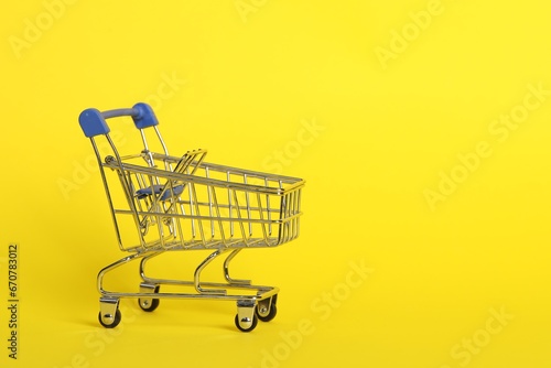 Small metal shopping cart on yellow background. Space for text