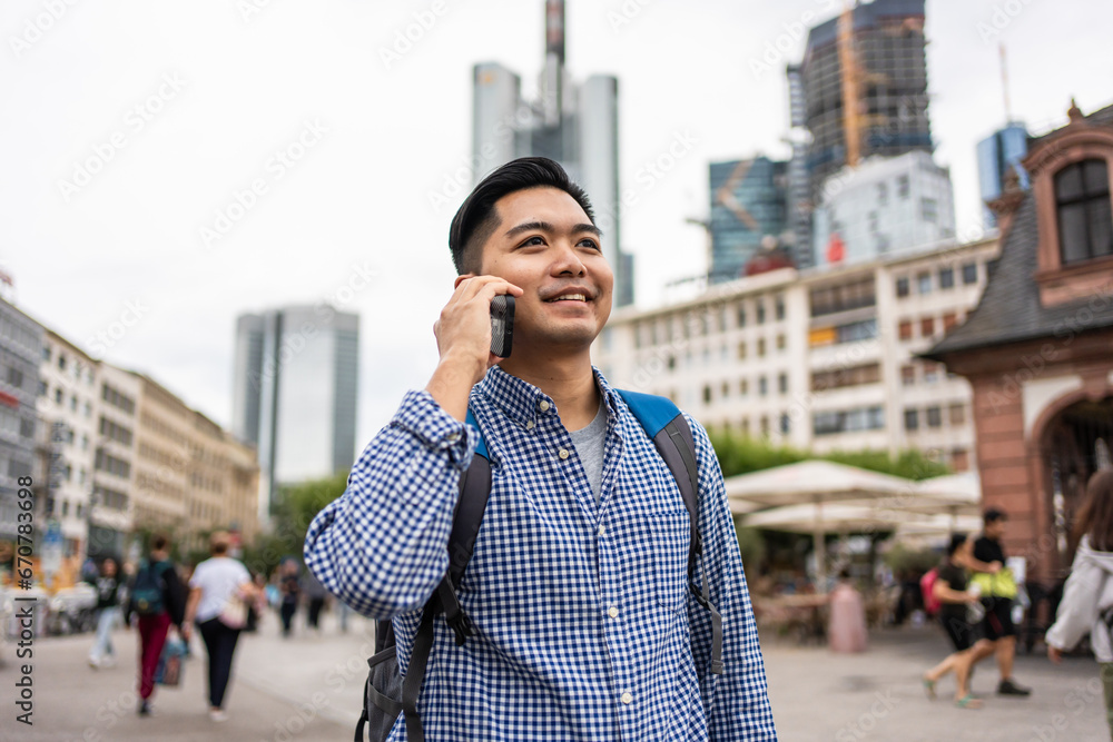 Asian young man backpacker talking on the phone while walking in city. 