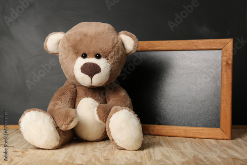 Teddy bear and small blackboard on wooden table. Space for text