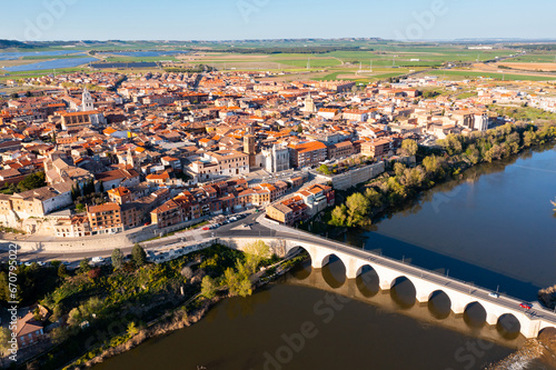 Picturesque aerial view of Tordesillas townscape on Duero river overlooking brownish tiled roofs of residential buildings and temples on spring day, Spain