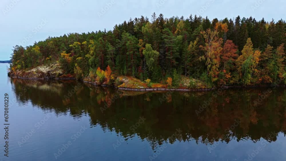 Autumn forest on a lakeshore with green, brown, red and yellow trees reflected on the lake in Valkeakoski, Finland. Camera moving left. Autumn forest on a lakeshore with green, brown, red and yellow trees reflected on the lake in Valkeakoski, Finland. Camera moving left.